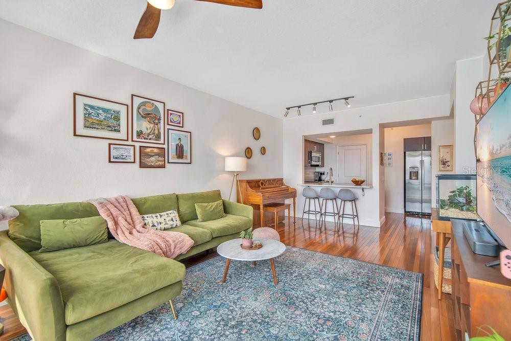 A living room features a green sectional sofa, a piano, and a rug on hardwood floors — 322 E CENTRAL BOULEVARD UNIT 1005, ORLANDO, FL