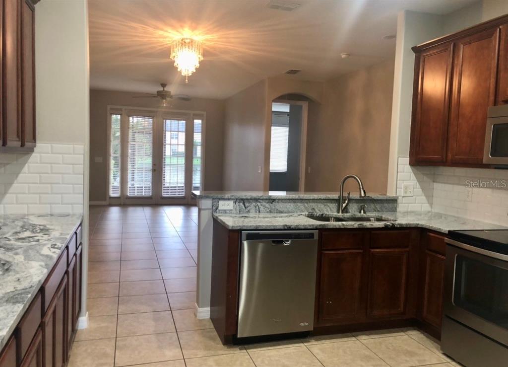 A kitchen with dark wood cabinets, granite countertops, and stainless steel appliances overlooks a living area — 540 WOODLAND TERRACE BOULEVARD, ORLANDO, FL