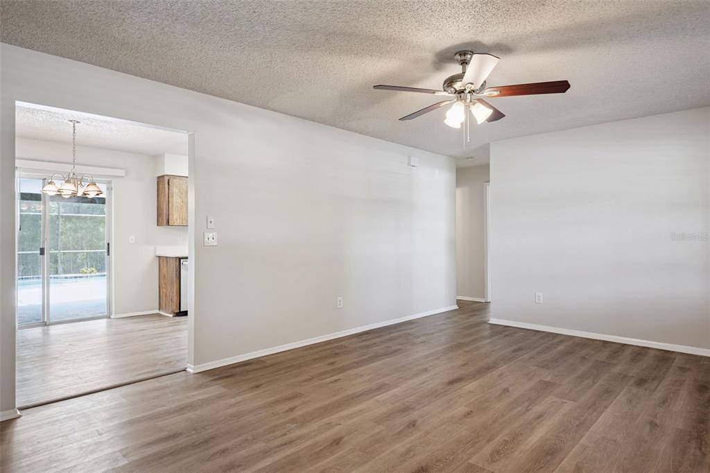 An empty living room with wood-look flooring, a ceiling fan, and a view into a kitchen — 111 BORADA ROAD, SANFORD, FL
