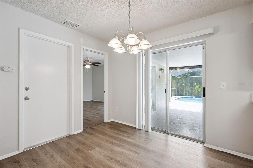 A dining area with wood-look flooring, a chandelier, and sliding glass doors leading to a pool — 111 BORADA ROAD, SANFORD, FL