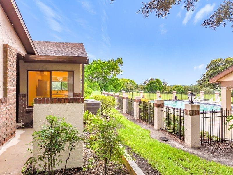 A view of a house exterior, a small garden, and a fenced swimming pool area — 340 GOLFSIDE COVE UNIT 340, LONGWOOD, FL