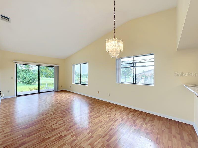 A bright living room features vaulted ceilings, wood-look flooring, a crystal chandelier, and sliding doors — 340 GOLFSIDE COVE UNIT 340, LONGWOOD, FL