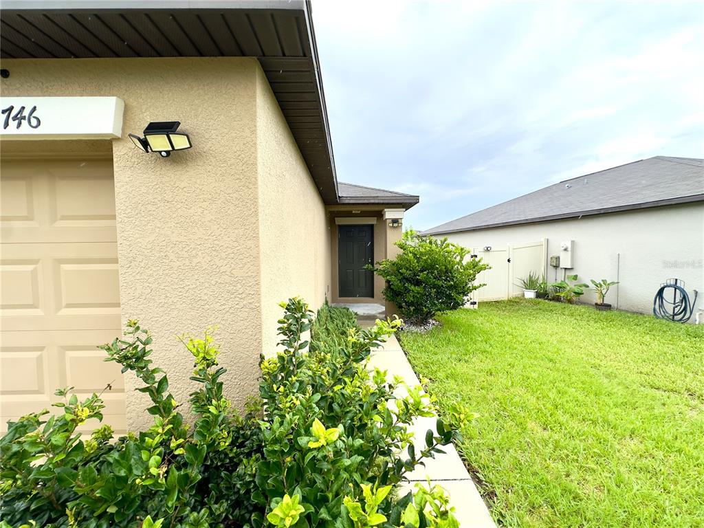 A side view of a house exterior showing a garage, a walkway, and a lawn — 9746 SAGE CREEK DRIVE, RUSKIN, FL