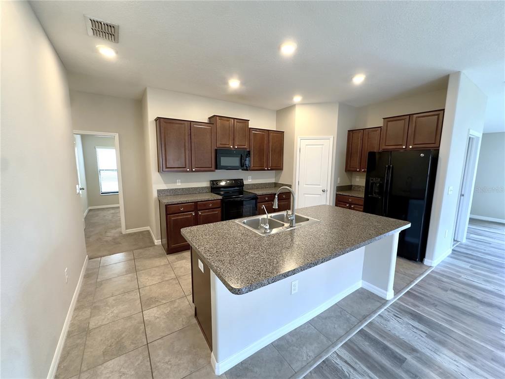 A kitchen features dark wood cabinets, granite countertops, a center island, and black appliances — 9746 SAGE CREEK DRIVE, RUSKIN, FL