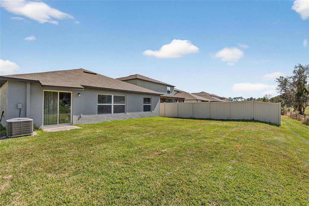 The backyard of a single-story house features a grassy lawn and a vinyl privacy fence — 1748 RED LOOP, LAKELAND, FL
