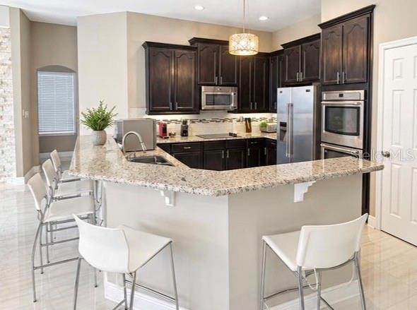A kitchen features dark wood cabinets, granite countertops, stainless steel appliances, and a breakfast bar — 10133 FACET COURT, ORLANDO, FL