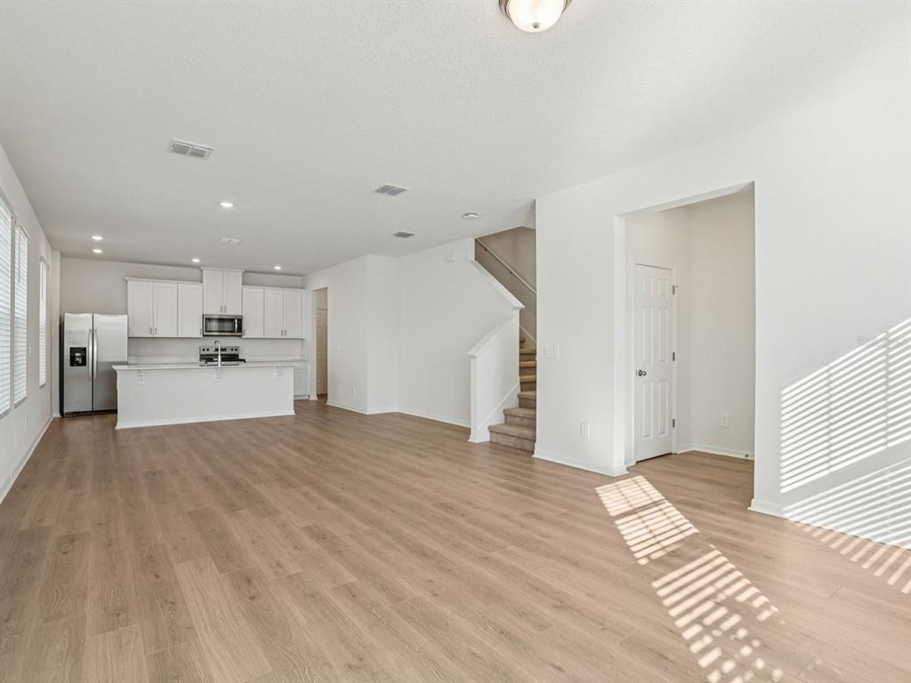 An open-concept living area features light wood-look flooring, white walls, and a kitchen with white cabinets — 4676 HOMESTEAD TRAIL, ST CLOUD, FL