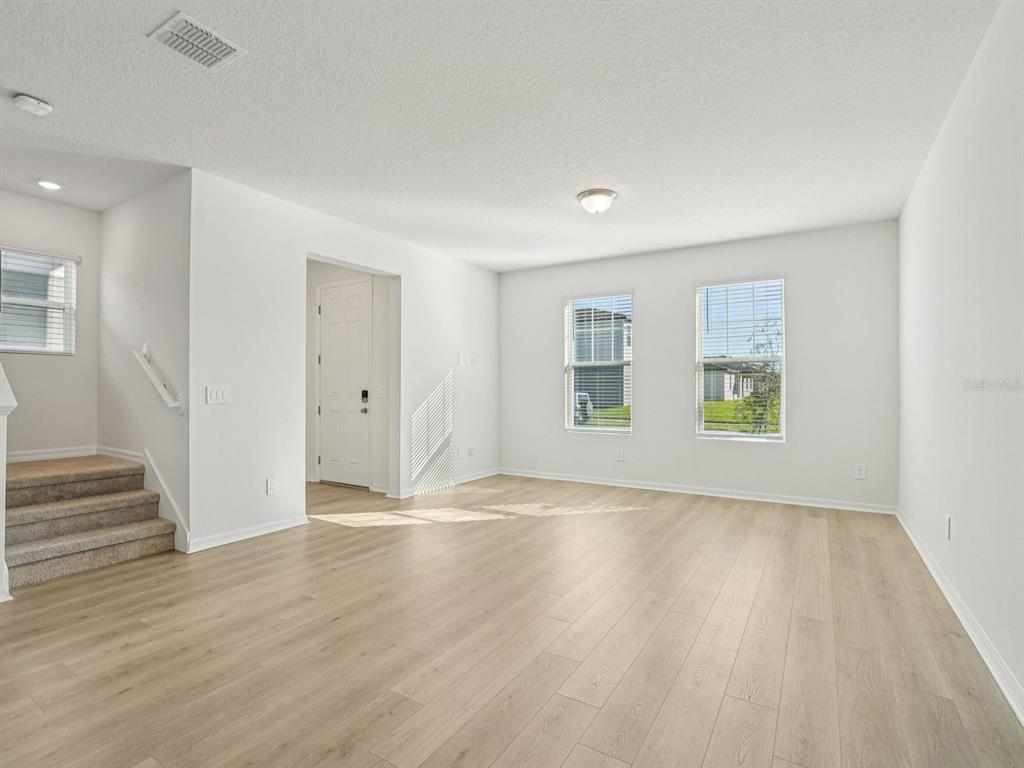 An empty living room features light wood-look flooring, white walls, and stairs on the left — 4676 HOMESTEAD TRAIL, ST CLOUD, FL