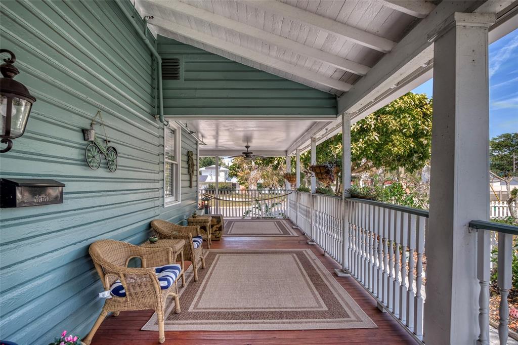 A covered wooden porch features wicker chairs, area rugs, and a white railing — 304 15TH STREET W, BRADENTON, FL
