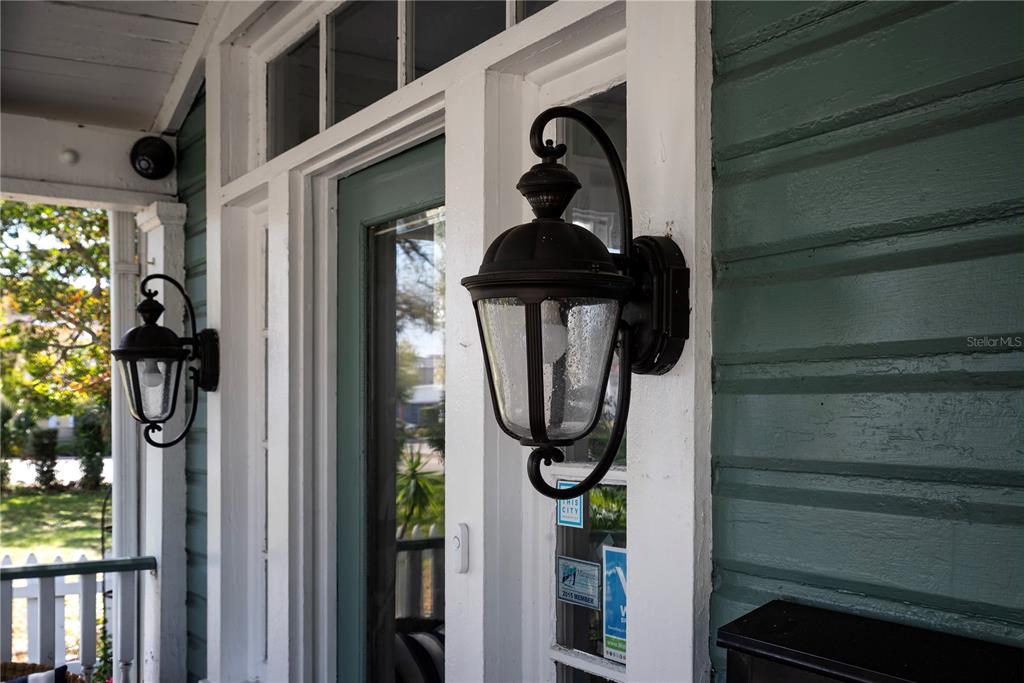 A close-up view of a porch featuring two black wall-mounted lanterns and teal siding — 304 15TH STREET W, BRADENTON, FL