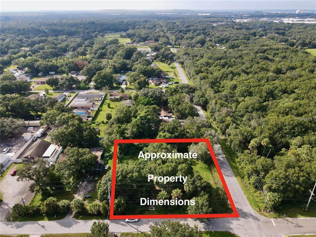 An aerial view shows a rectangular, wooded vacant lot outlined in red beside a paved road — 5803 12TH AVENUE S, TAMPA, FL