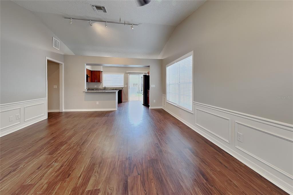 A living room with wood-look flooring, white wainscoting, and a view into the kitchen — 4514 CABBAGE PALM DRIVE, VALRICO, FL