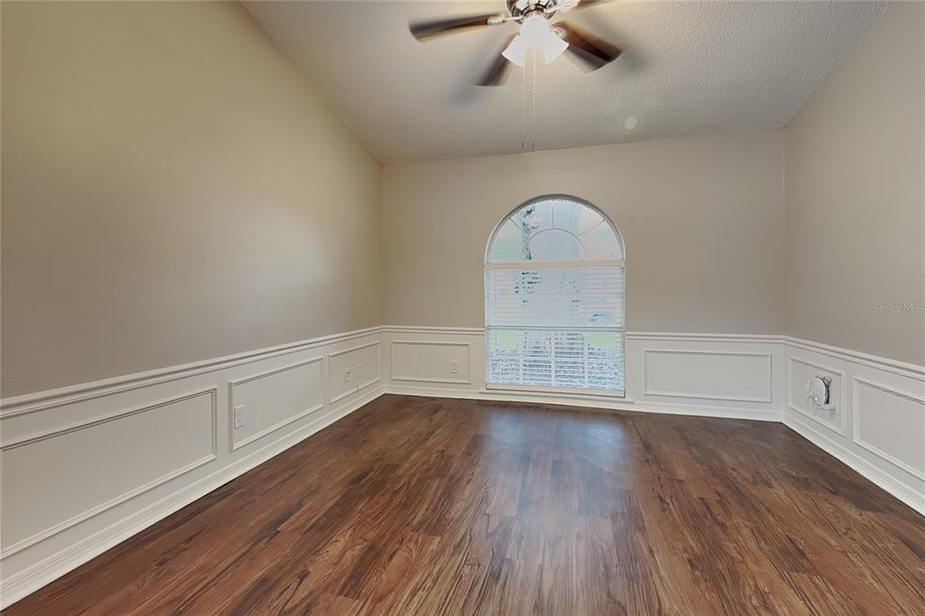 An empty room with wood-look flooring, white wainscoting, a ceiling fan, and an arched window — 4514 CABBAGE PALM DRIVE, VALRICO, FL