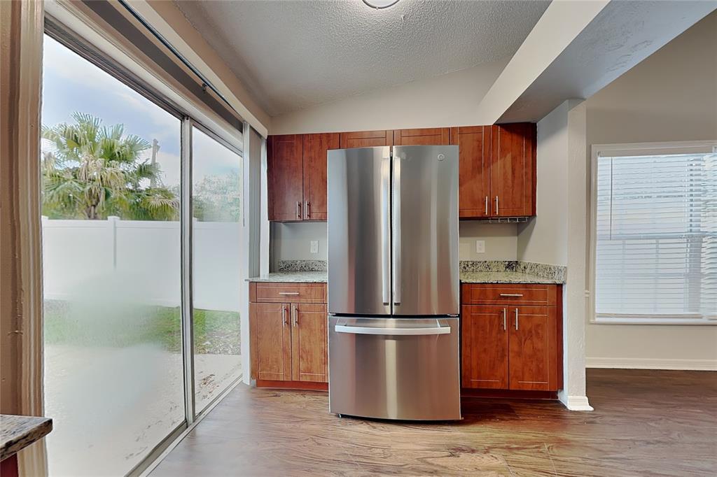 A kitchen area features wood cabinets, granite countertops, a stainless steel refrigerator, and sliding glass doors — 4514 CABBAGE PALM DRIVE, VALRICO, FL
