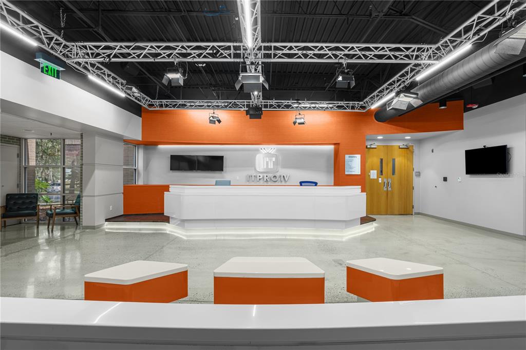 A modern office reception area features a white desk, orange accent walls, and industrial lighting — 7525 NW 4TH BOULEVARD, GAINESVILLE, FL
