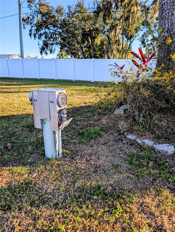 An outdoor utility pedestal stands in a grassy yard near a white vinyl fence — 3275 26TH AVENUE E UNIT 55, BRADENTON, FL