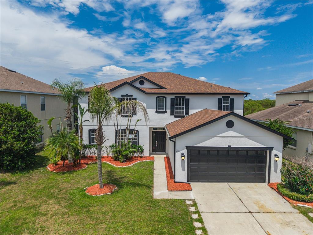 A two-story house with white stucco walls, a brown shingled roof, and a two-car garage — 2321 THE OAKS BOULEVARD, KISSIMMEE, FL