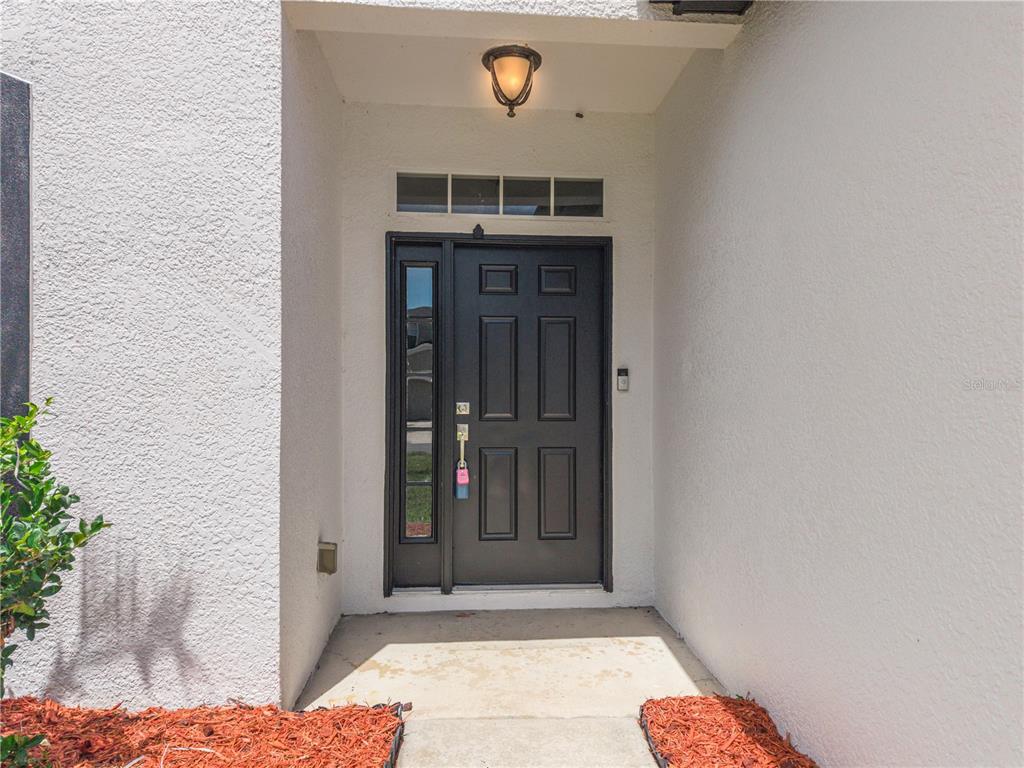 A black front door with a side window is set within a white stucco entryway — 2321 THE OAKS BOULEVARD, KISSIMMEE, FL