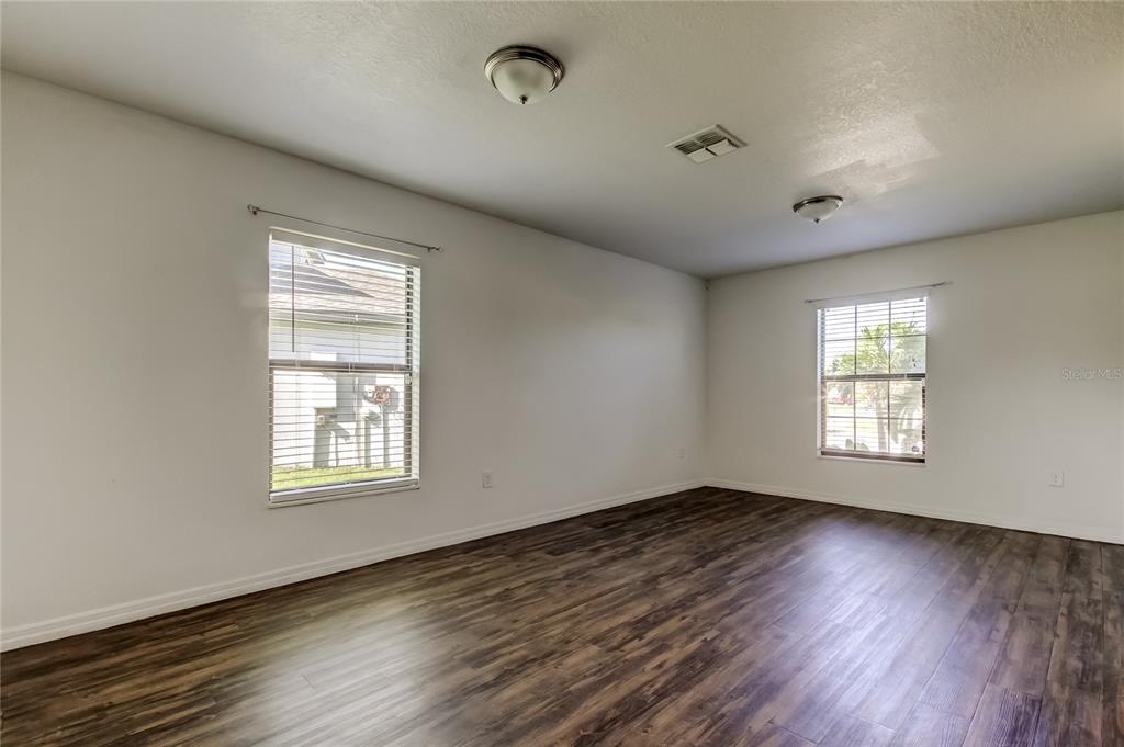 An empty room features white walls, dark wood-look flooring, two windows, and two ceiling lights — 1739 CHATHAM GREEN CIRCLE, RUSKIN, FL