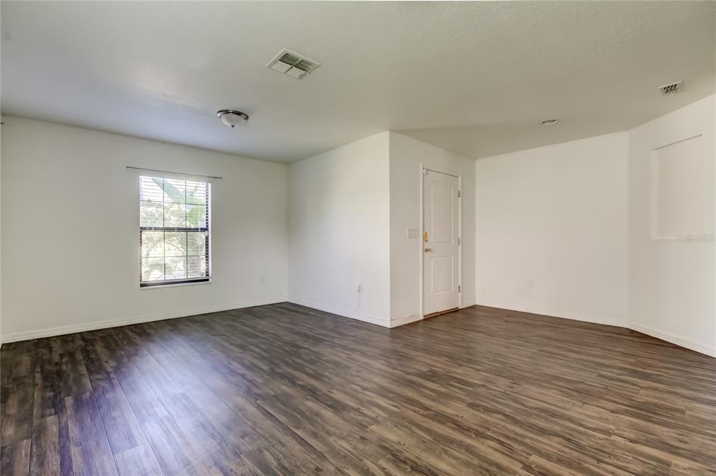 An empty room features white walls, dark wood-look flooring, a window, and a white door — 1739 CHATHAM GREEN CIRCLE, RUSKIN, FL