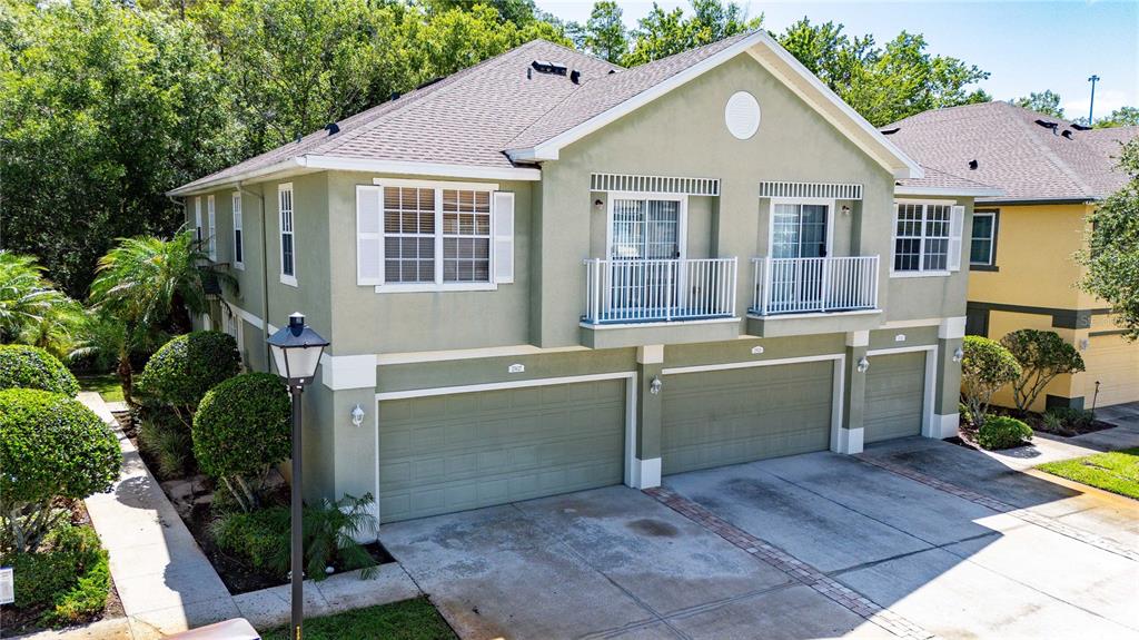 An exterior view of a two-story residential building featuring three garage doors and two balconies — 27627 PLEASURE RIDE LOOP, WESLEY CHAPEL, FL