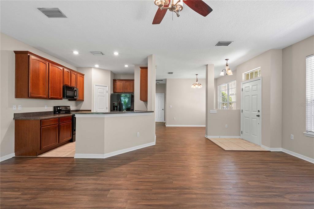 An open-concept kitchen with wood cabinets and dark countertops overlooks a living area with flooring — 27627 PLEASURE RIDE LOOP, WESLEY CHAPEL, FL