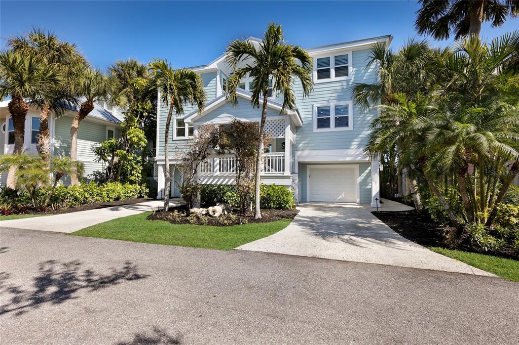 A light blue, multi-story coastal home features a white garage, front porch, and palm trees — 585 BUTTONWOOD BAY DRIVE, BOCA GRANDE, FL