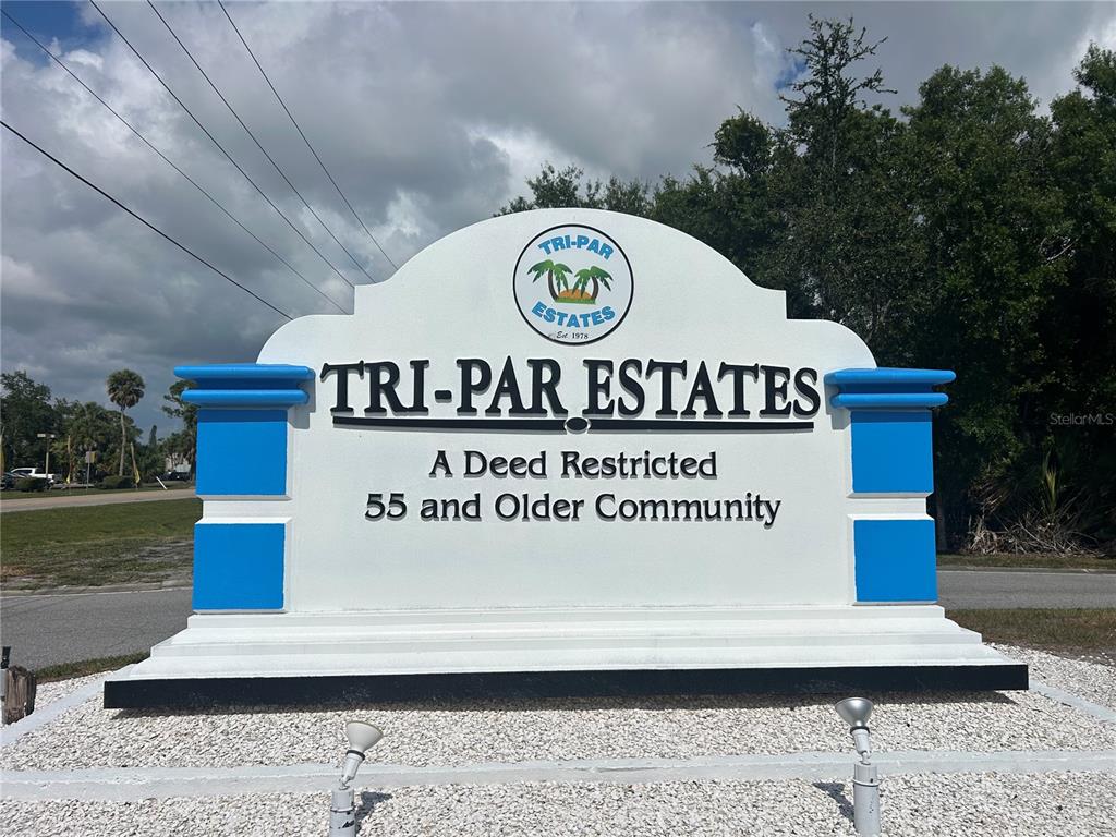 A white monument sign for Tri-Par Estates stands in a gravel bed under a cloudy sky — 5325 BOCA RATON AVENUE, SARASOTA, FL