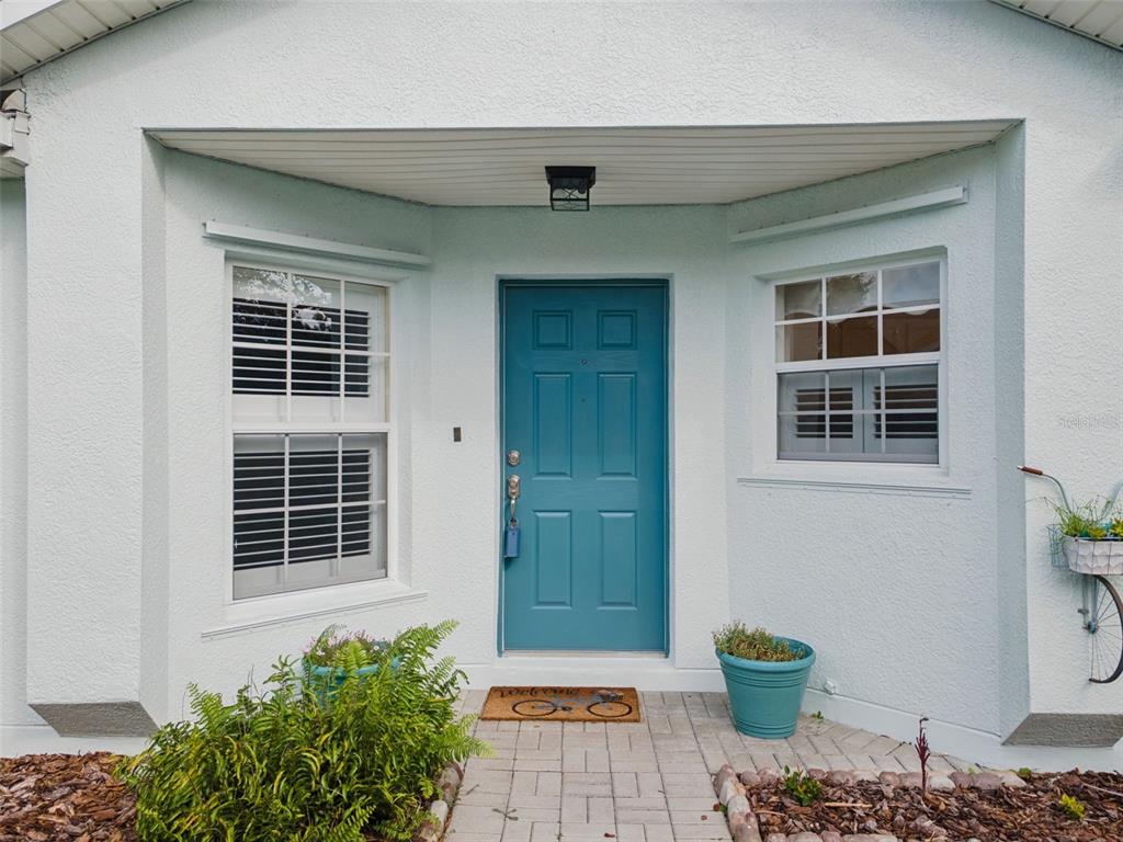 A teal front door is centered between two windows on a light-colored stucco house exterior — 205 BELL TOWER CROSSING WEST, KISSIMMEE, FL