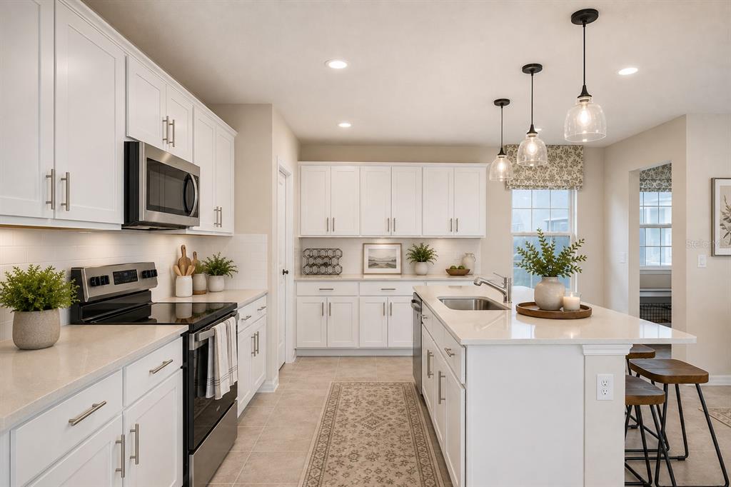 A bright kitchen features white cabinetry, quartz countertops, a center island, and stainless steel appliances — 10876 WATERWOOD ALLEY, ORLANDO, FL
