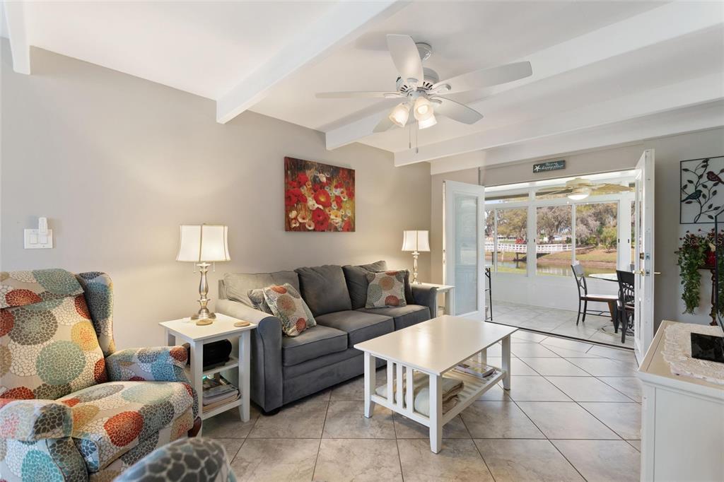 A living room with tile floors, a gray sofa, patterned armchair, and a sunroom view — 1919 CLUB CIRCLE, LAKESHORE, FL