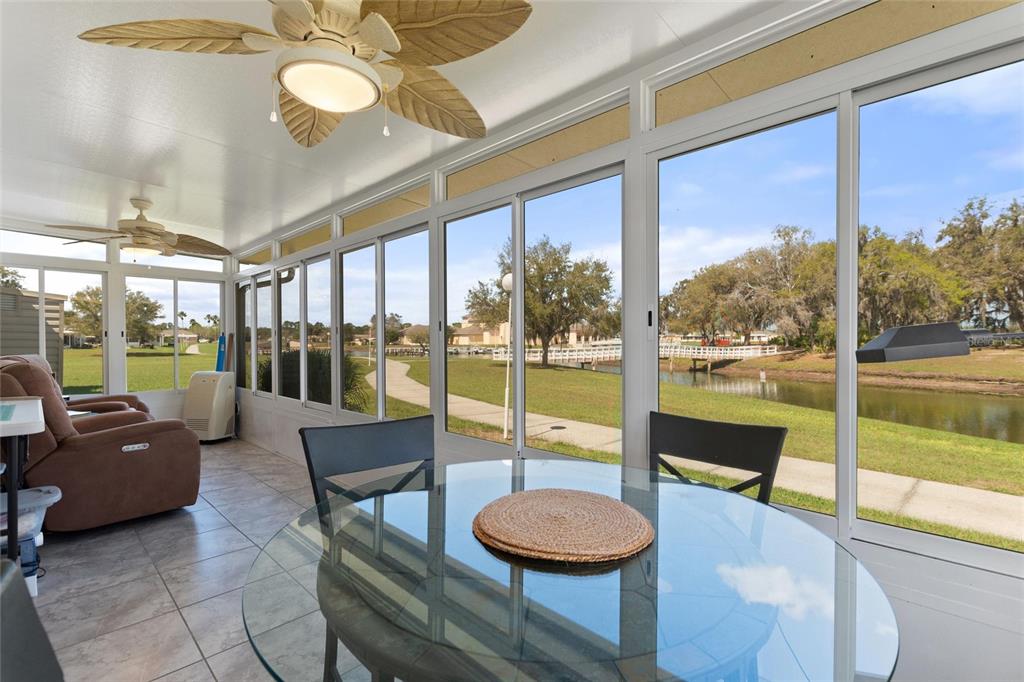 A sunroom with tile floors, a glass dining table, and views of a pond outside — 1919 CLUB CIRCLE, LAKESHORE, FL