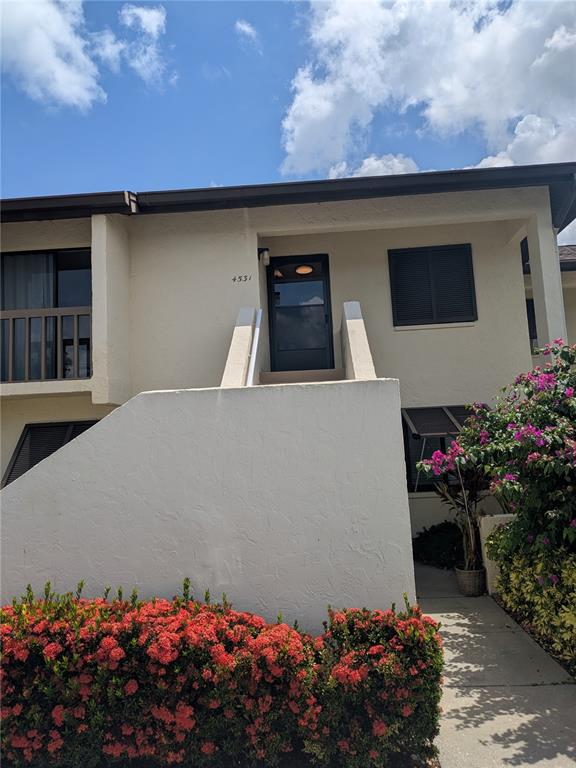 A two-story building exterior features a white stucco facade, a dark front door, and landscaping — 4531 LONGWATER UNIT 16, SARASOTA, FL