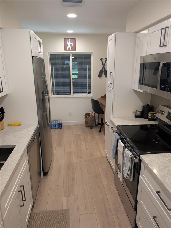 A galley kitchen features white cabinets, stainless steel appliances, light wood-look flooring, and a window — 4531 LONGWATER UNIT 16, SARASOTA, FL