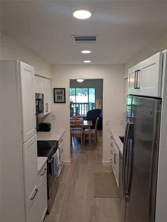 A galley kitchen features white cabinets, stainless steel appliances, and light wood-look flooring — 4531 LONGWATER UNIT 16, SARASOTA, FL