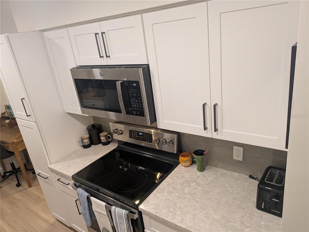 A kitchen features white cabinets, stainless steel appliances, a glass-top stove, and light-colored countertops — 4531 LONGWATER UNIT 16, SARASOTA, FL