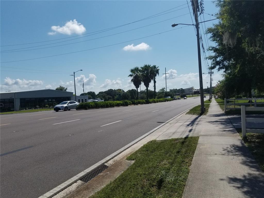 A view of a multi-lane road with a sidewalk, palm trees, and a commercial building — 2050 HAVENDALE BOULEVARD NW UNIT B, WINTER HAVEN, FL