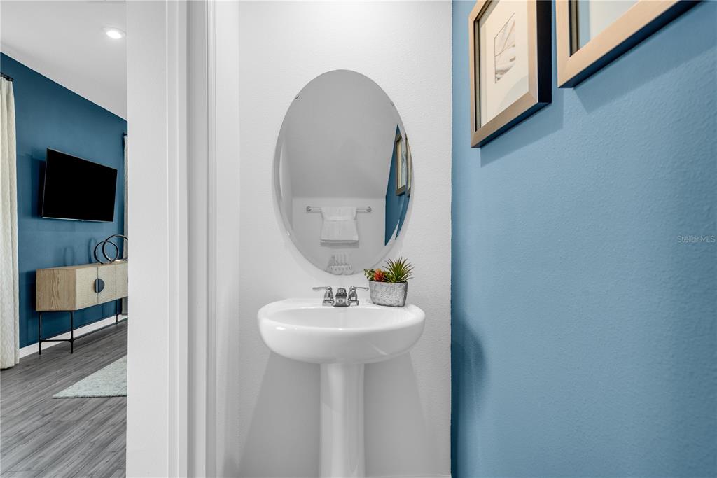 A powder room features a white pedestal sink, an oval mirror, and blue walls — 906 CASTLEFORD AVENUE, PALM BAY, FL