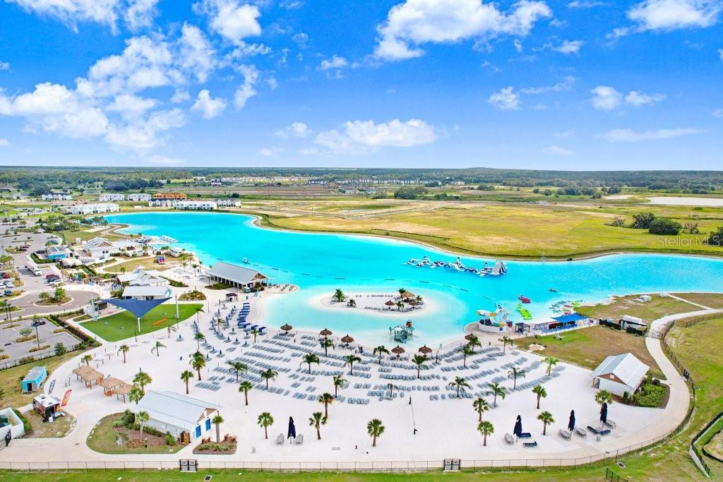 An aerial view of a large man-made turquoise lagoon with a sandy beach and palm trees — 11099 RADIANT SHORE LOOP, SAN ANTONIO, FL
