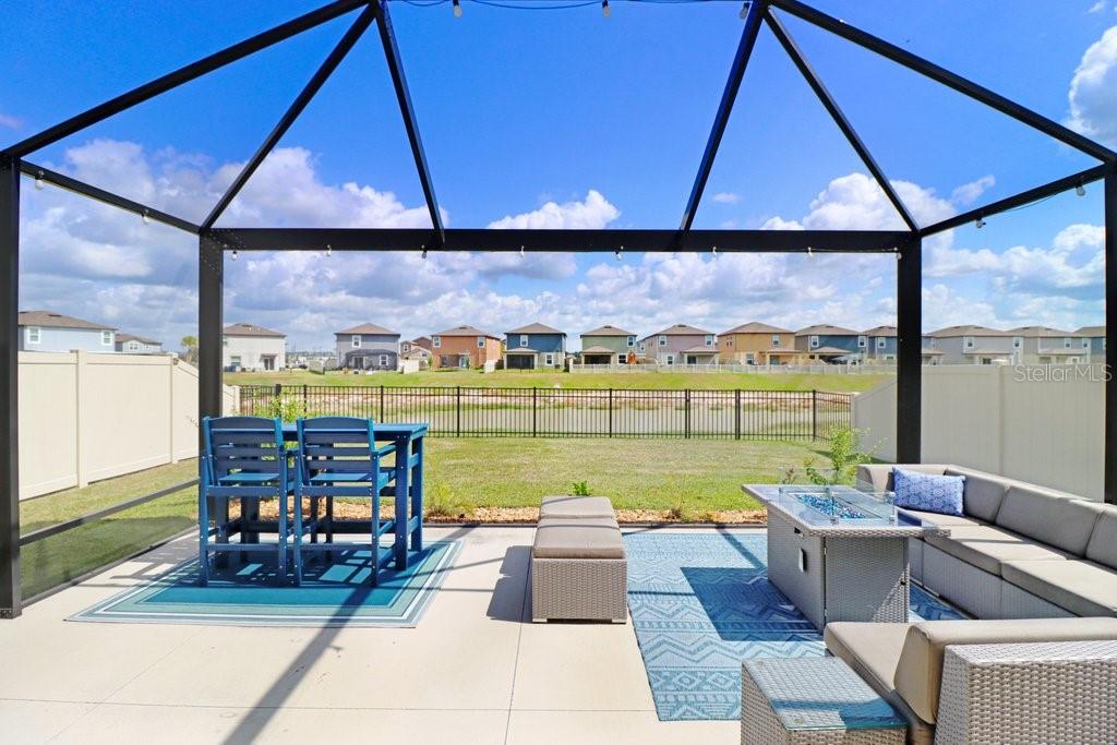 A screened-in patio features outdoor furniture, a fire pit table, and a view of houses — 11099 RADIANT SHORE LOOP, SAN ANTONIO, FL