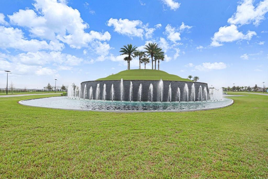 A large circular fountain with tiered landscaping and palm trees sits in a grassy field — 11099 RADIANT SHORE LOOP, SAN ANTONIO, FL