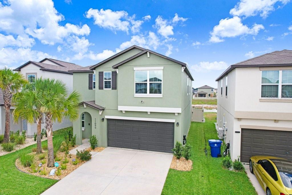 A two-story green house with a two-car garage and a concrete driveway — 11099 RADIANT SHORE LOOP, SAN ANTONIO, FL