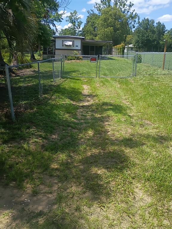 A chain-link fence with a double gate encloses a grassy yard leading to a mobile home — 37247 NORTHSIDE DRIVE, ZEPHYRHILLS, FL