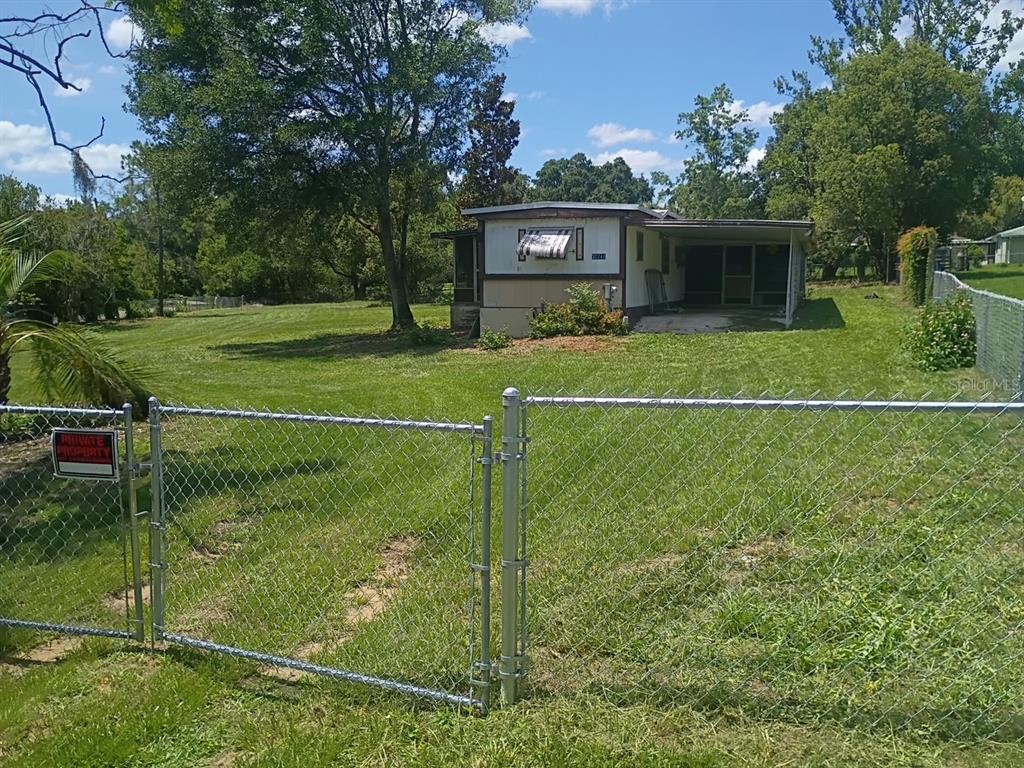 A mobile home with a screened-in porch sits on a grassy lot behind a chain-link fence — 37247 NORTHSIDE DRIVE, ZEPHYRHILLS, FL