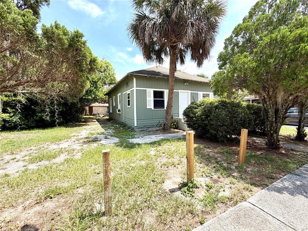 A single-story green house with white trim stands behind wooden posts in a grassy yard — 209 AVENUE C NE, WINTER HAVEN, FL