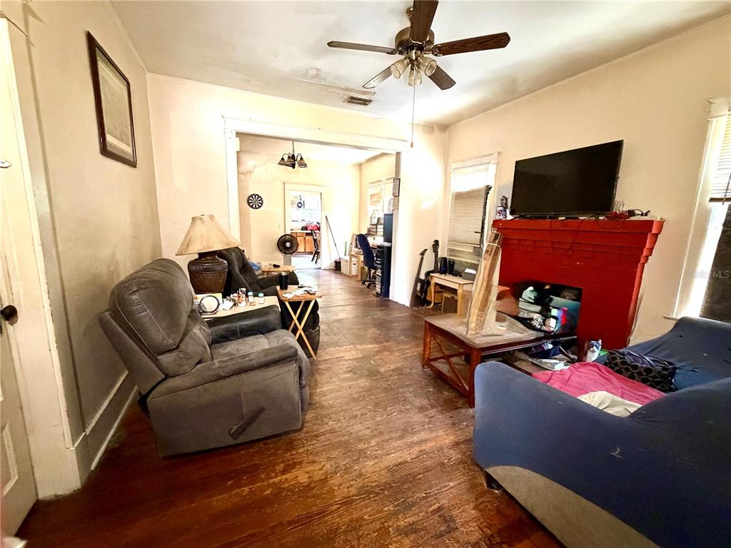 A living room features hardwood floors, a red fireplace, a ceiling fan, and gray furniture — 209 AVENUE C NE, WINTER HAVEN, FL