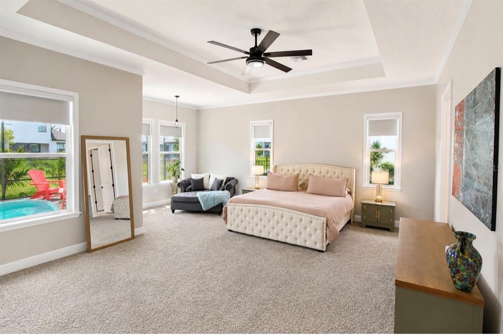 A spacious bedroom features a tufted bed, a seating area, and a view of a pool — 8197 GULLEN DRIVE, MELBOURNE, FL