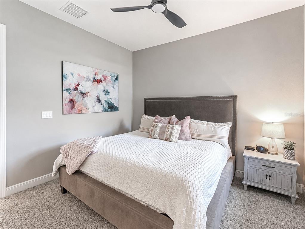 A bedroom features a gray upholstered bed, a white textured quilt, and a nightstand — 8197 GULLEN DRIVE, MELBOURNE, FL