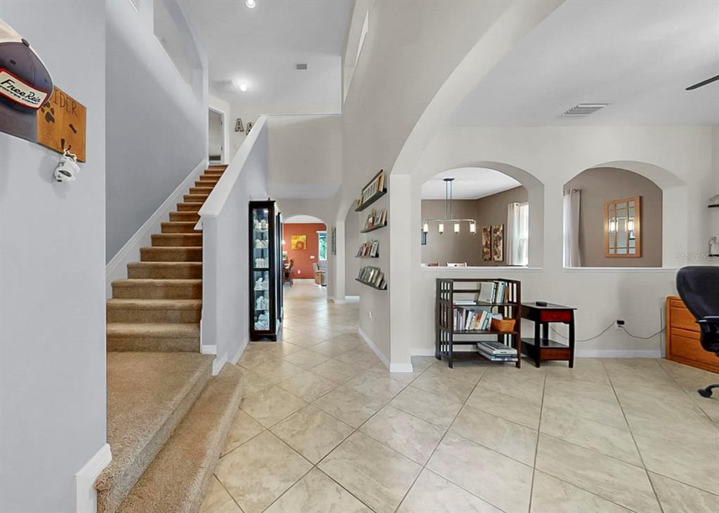 A tiled entryway features a carpeted staircase, arched wall openings, and a tall display cabinet — 2927 130TH AVENUE E, PARRISH, FL