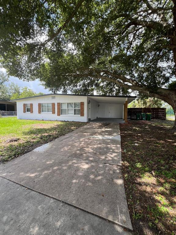 A white single-story house with a concrete driveway, carport, and large oak tree in front — 1221 CYPRESS LANE, COCOA, FL
